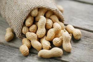 Peanuts in a miniature burlap bag on old, gray wooden surface photo