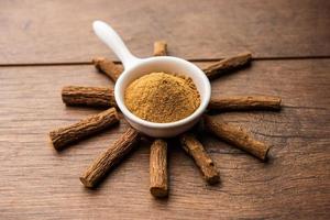 Ayurvedic Mulethi or Liquorice root stick or jeshthamadh powder served in a bowl over moody background photo