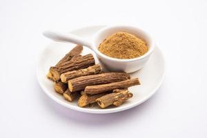 Ayurvedic Mulethi or Liquorice root stick or jeshthamadh powder served in a bowl over moody background photo