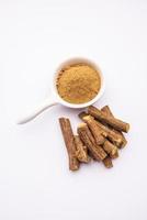 Ayurvedic Mulethi or Liquorice root stick or jeshthamadh powder served in a bowl over moody background photo