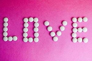 Beautiful inscription love made from white round smooth medical pills, vitamins, antibiotics and copy space on a bright purple pink background. Flat lay photo