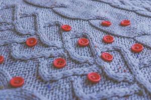 Beautiful texture of a soft warm natural sweater with a knitted pattern of yarn and red small round buttons for sewing. The background photo