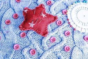 Beautiful texture of a soft warm natural sweater, knitted fabrics and red small round buttons for sewing and a needle pad. Flat lay. The background photo