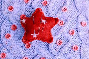 Beautiful texture of a soft warm natural sweater, knitted fabrics and red small round buttons for sewing and a needle pad. Flat lay. The background photo