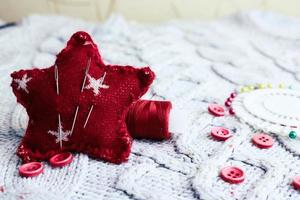 Beautiful texture of a soft warm natural sweater, fabrics with a knitted pattern and red small round buttons for sewing and a skein of thread, needle bed and needle pad. Flat lay. The background photo