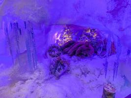 escena de diseño festivo un oso de juguete duerme en una guarida cubierta de nieve, un árbol decorado detrás de él. carámbanos decoran la entrada de la guarida. foto