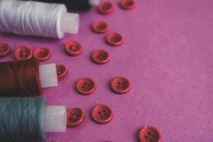 hermosa textura con muchos botones rojos redondos para coser, coser y madejas de carretes de hilo. copie el espacio endecha plana rosa, fondo morado