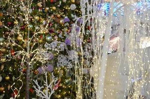 shop window decoration, shopping center decor. artificial white spruce with garlands. near there are white trees with yellow lights garlands. spruce branches in stylish decorations photo