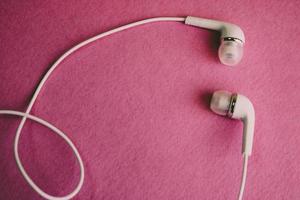 Beautiful modern digital plastic vacuum white headphones with wires for listening to music on a purple pink background. Copy space photo