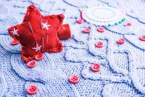 hermosa textura de un suéter natural cálido y suave, telas con un patrón de punto y pequeños botones rojos redondos para coser y una madeja de hilo, cama de aguja y almohadilla de aguja. endecha plana el fondo foto