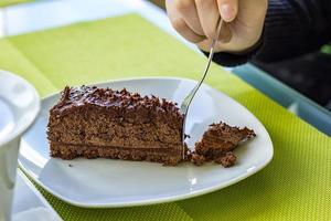 A girl's hand breaks a piece of chocolate cake on a plate. photo