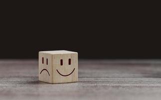 concepto de salud mental y estado emocional, cara sonriente en el lado brillante y cara triste en el lado oscuro en un cubo de madera para una selección de mentalidad positiva. foto