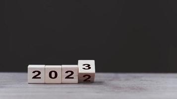 Banner de concepto de feliz año nuevo 2023. volteando el calendario de números de 2022 a 2023 en bloques de cubo de madera aislados en fondo oscuro para el cambio de año nuevo para comenzar cosas nuevas o nuevos negocios. foto