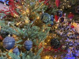 Green branches of a fluffy Christmas festive New Year tree with toys in balls and bright glowing light bulbs and garlands, background photo