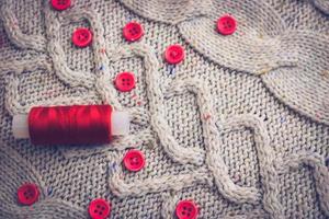 hermosa textura de un suéter natural cálido y suave, telas con un patrón de punto de hilo y pequeños botones redondos rojos para coser y una madeja de hilo rojo. el fondo foto
