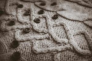 Beautiful texture of a soft warm natural sweater with a knitted pattern of yarn and black and white small round buttons. The background photo