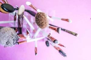 A set of beautiful different soft brushes for make-up from natural nap for beauty targeting and applying a tonal foundation in a stand and copy space on a pink, purple background photo