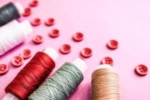 Beautiful texture with lots of round red buttons for sewing, needlework and skeins of spools of thread. Copy space. Flat lay. Pink, purple background photo