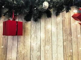 Small cute red festive gift boxes, Christmas, New Year's decoration on the background of green Christmas-tree branches with needles and glowing garlands on wooden vertical boards with seams photo