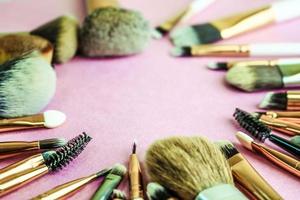 A frame from a set of beautiful different soft makeup brushes from natural lint for targeting beauty and applying a tonal base in a stand and copy space on a pink, purple background photo
