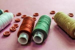 Beautiful texture with lots of round red buttons for sewing, needlework and skeins of spools of thread. Copy space. Flat lay. Pink, purple background photo