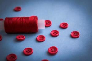 hermosa textura con muchos botones rojos redondos para coser, costura y una bobina de hilo. copie el espacio endecha plana fondo azul foto