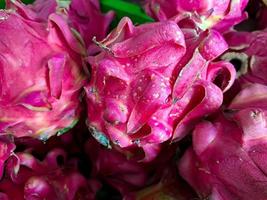 manojo de fruta de dragón dulce roja. varias frutas de dragón rojas dulces grandes puestas en una mesa de madera sobre fondo natural para la venta en una tienda de frutas foto