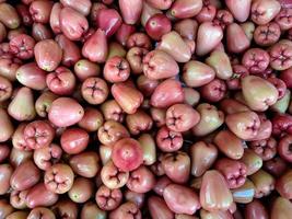 manojo de guayaba de agua roja dulce varias frutas colocadas sobre una mesa de madera sobre fondo natural a la venta en una frutería foto