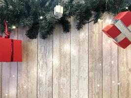 Small cute red festive gift boxes, Christmas, New Year's decoration on the background of green Christmas-tree branches with needles and glowing garlands on wooden vertical boards with seams photo