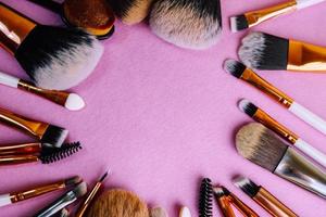 un marco de un conjunto de hermosos pinceles de maquillaje suave diferentes de pelusa natural para enfocarse en la belleza y aplicar una base tonal en un espacio de soporte y copia sobre un fondo rosa, púrpura foto