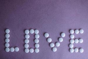 Beautiful inscription love made from white round smooth medical pills, vitamins, antibiotics and copy space on a bright purple pink background. Flat lay photo