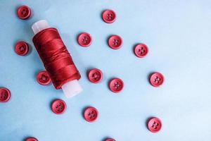 Beautiful texture with lots of round red buttons for sewing, needlework and a coil of thread. Copy space. Flat lay. Blue background photo