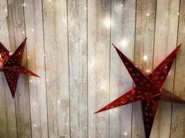grandes y lindas estrellas rojas navideñas, navidad, decoración de año nuevo contra el fondo de gerlyand brillante sobre tablas verticales de madera con costuras foto