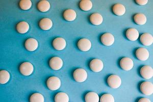 Beautiful texture with white round smooth medical pills, vitamins, antibiotics and copy space on a blue background. Flat lay photo