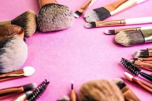 A frame from a set of beautiful different soft makeup brushes from natural lint for targeting beauty and applying a tonal base in a stand and copy space on a pink, purple background photo