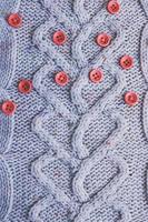 Beautiful texture of a soft warm natural sweater with a knitted pattern of yarn and red small round buttons for sewing. The background photo