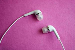 hermosos y modernos audífonos blancos al vacío de plástico digital con cables para escuchar música sobre un fondo rosa púrpura. copie el espacio foto
