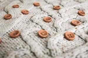 Beautiful texture of a soft warm natural sweater with a knitted pattern of yarn and red small round buttons for sewing. The background photo