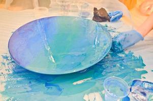 A man in a blue glove beautifully paints draws an acrylic blue multi-colored resin a round home-made board photo