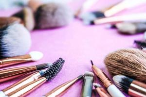 A frame from a set of beautiful different soft makeup brushes from natural lint for targeting beauty and applying a tonal base in a stand and copy space on a pink, purple background photo