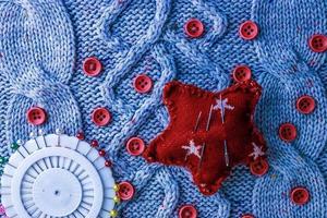 Beautiful texture of a soft warm natural sweater, knitted fabrics and red small round buttons for sewing and a needle pad. Flat lay. The background photo