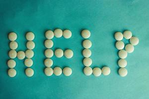 Beautiful inscription help made from white round smooth medical pills, vitamins, antibiotics and copy space on a bright blue background. Flat lay photo