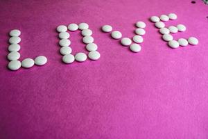 Beautiful inscription love made from white round smooth medical pills, vitamins, antibiotics and copy space on a bright purple pink background. Flat lay photo