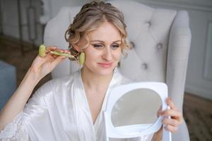 Beautiful woman in silk robe using jade face roller with natural stones doing photo