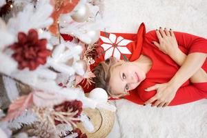 High angle view young woman lying on floor near Christmas tree with gifts. Top photo