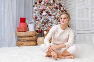 joven hermosa mujer sentada en el piso cerca del árbol de navidad y presenta el año nuevo foto