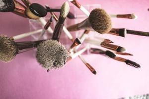 A set of beautiful different soft brushes for make-up from natural nap for beauty targeting and applying a tonal foundation in a stand and copy space on a pink, purple background photo