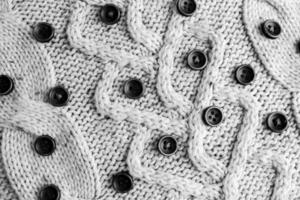 Beautiful texture of a soft warm natural sweater with a knitted pattern of yarn and black and white small round buttons. The background photo