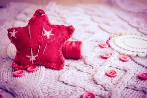 Beautiful texture of a soft warm natural sweater, fabrics with a knitted pattern and red small round buttons for sewing and a skein of thread, needle bed and needle pad. Flat lay. The background photo