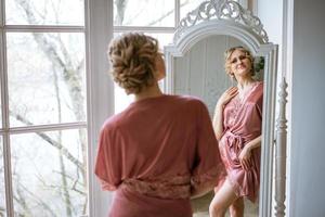 Beautiful woman in lace robe looks at her reflection in mirror while standing photo